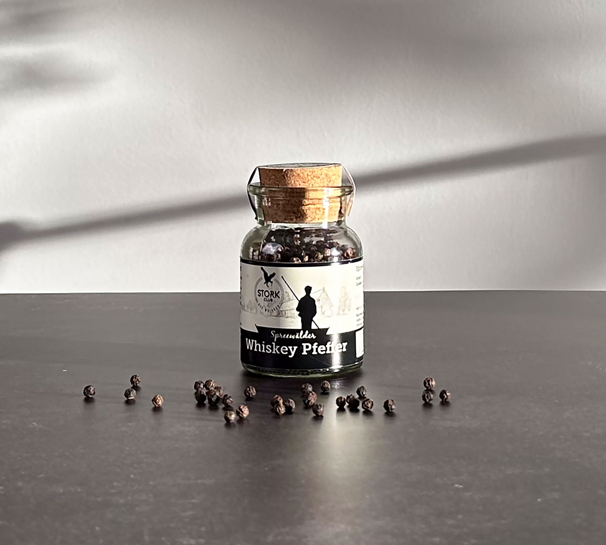 Whiskey Pfeffer im Korkglas. Vor dem Glas liegen Pfefferkörner.