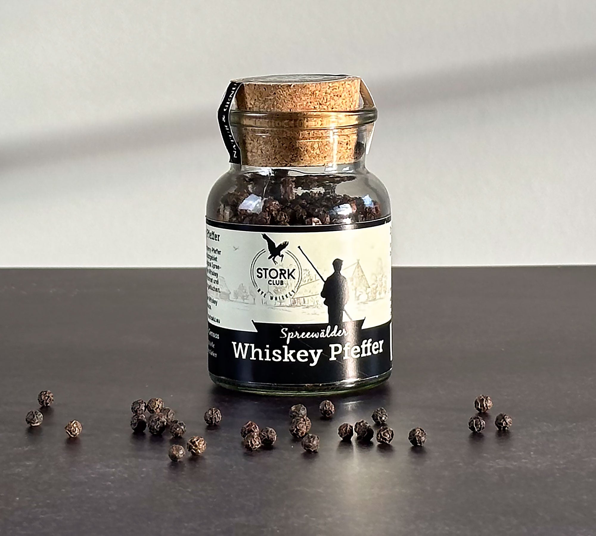 Whiskey Pfeffer im Korkglas. Vor dem Glas liegen Pfefferkörner.