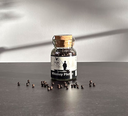 Whiskey Pfeffer im Korkglas. Vor dem Glas liegen Pfefferkörner.