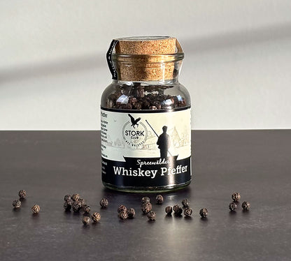 Whiskey Pfeffer im Korkglas. Vor dem Glas liegen Pfefferkörner.